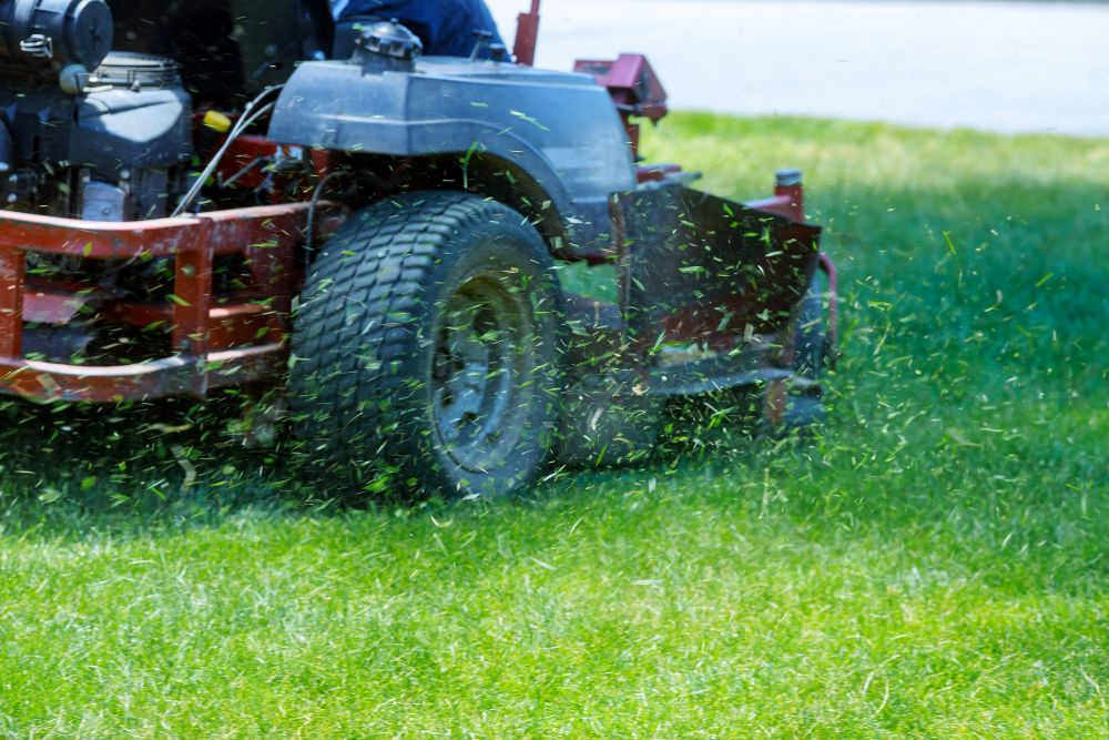 A lawn mower cutting grass in a green field under a clear blue sky.