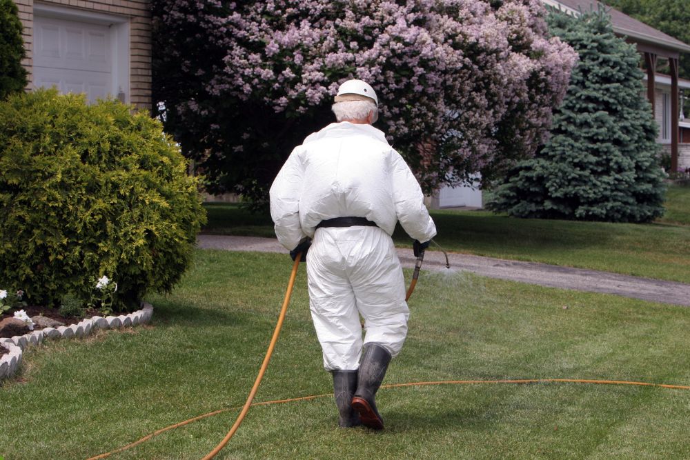 A man in a white suit and coveralls walks on green grass, showcasing a casual yet stylish appearance in an outdoor setting.