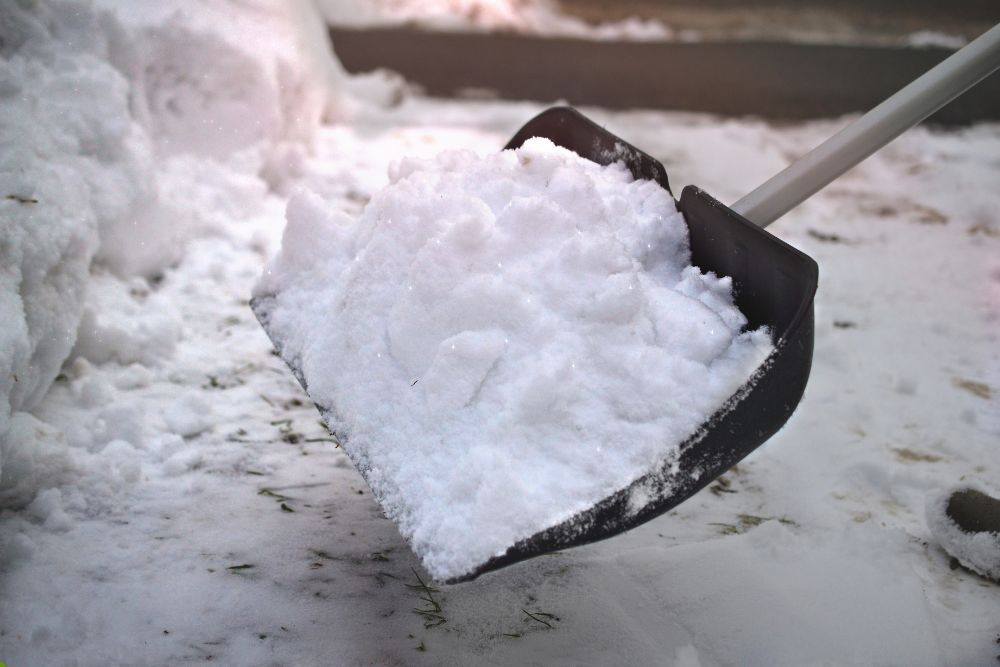 A shovel filled with freshly fallen snow resting on the ground, surrounded by a winter landscape.