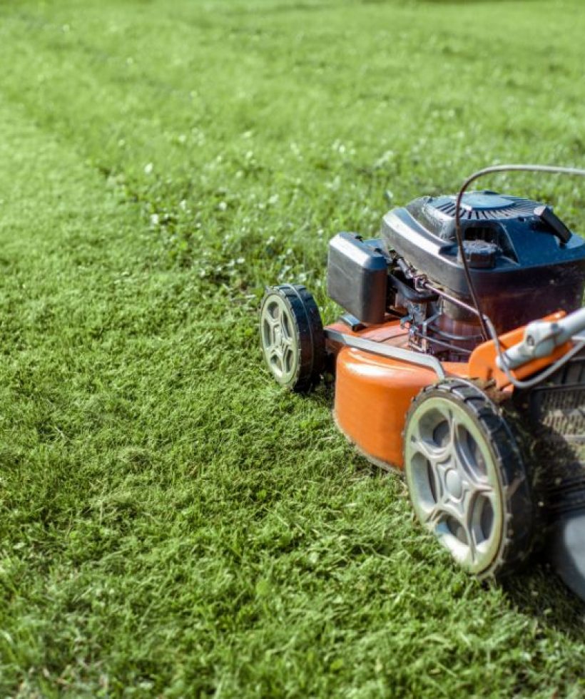 An orange lawn mower rests on a patch of green grass under clear skies.