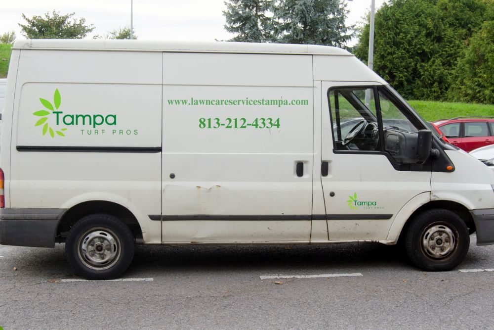 A white van with the Tampa Lawn Care logo, positioned on a suburban road.