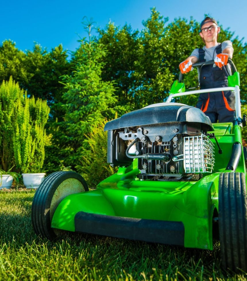 A man operates a green lawn mower, cutting grass in a well-maintained yard.